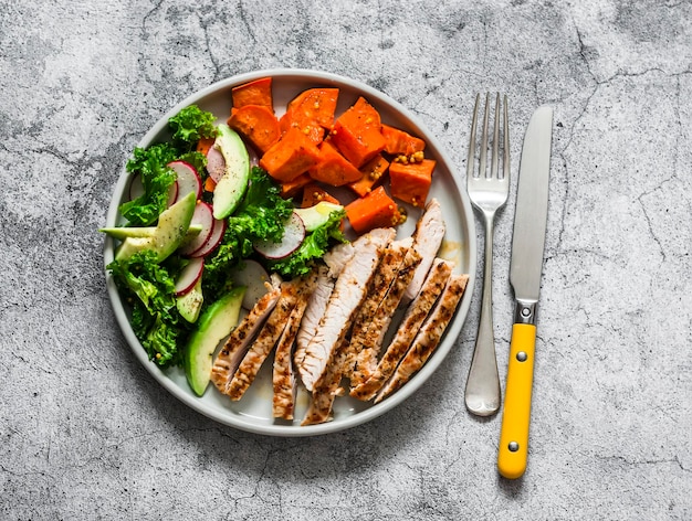 Evenwichtige voeding gegrilde kalkoen zoete aardappelen boerenkool kool avocado komkommers radijs salade op een grijze achtergrond bovenaanzicht