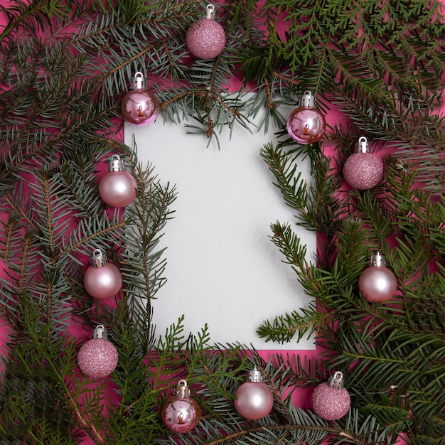 Evergreen trees with Christmas tree decorations on a pink background with copy space in white. Flat lay minimal scene.