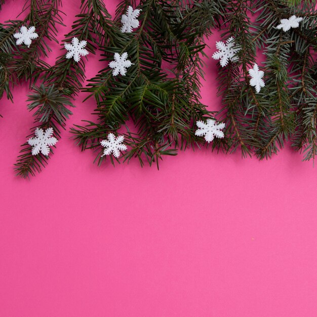 コピー スペースとピンクの背景に雪片を持つ常緑樹。フラットレイシーン。