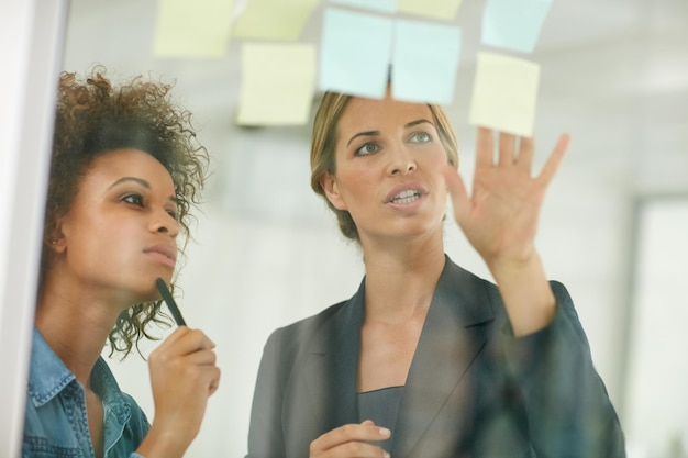 Photo every business follows a plan shot of coworkers using sticky notes against the wall during a brainstorming session