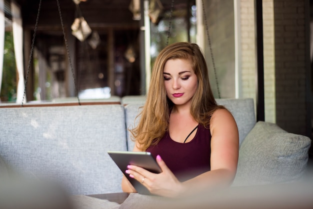 Everyday look. Plus size model. Beautiful young woman with a tablet in a restaurant.