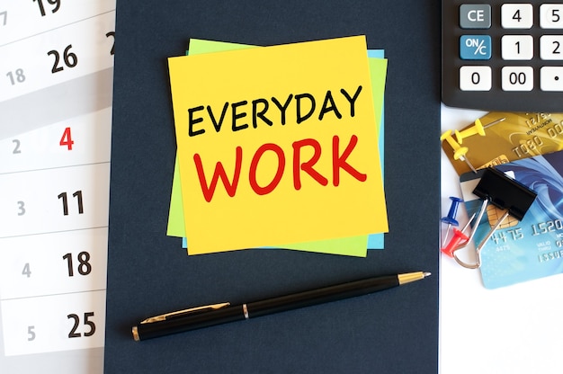 Everyday work, text on yellow paper square shape on a blue background. Notepad, calculator, credit cards, pen, stationery on the desktop. Business, financial and education concept. Selective focus.