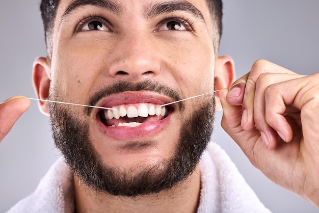 Все знают, как добиться ослепительной улыбки. Снимок молодого человека, чистящего зубы зубной нитью, стоя на сером фоне.
