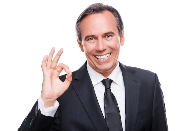 Everything is OK! Happy mature man in formalwear looking at camera and smiling while gesturing OK sign and standing against white background