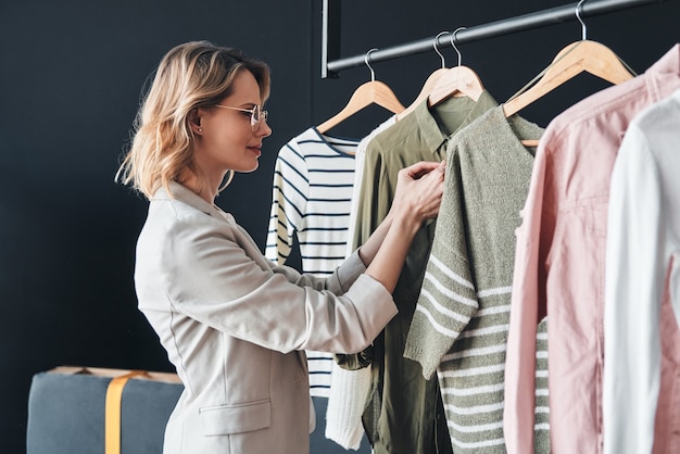 Everything is perfect. Attractive young woman in smart casual wear choosing clothes from the rank