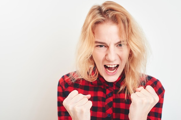 The evil blonde girl in red shirt on white background yells with your mouth open