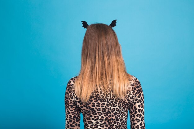 Photo the evil woman with a waist bat on the head. fancy dress for halloween on blue wall, back view