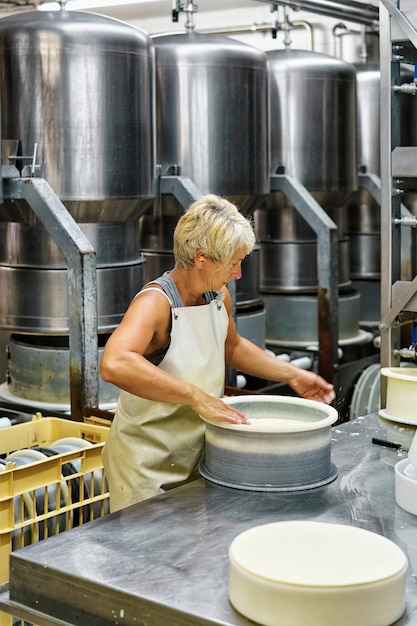 에빌레, 프랑스 - 2016년 8월 31일: 프랑스 부르고뉴 프랑슈 콩트의 낙농장에서 젊은 그뤼에르 드 콩트 치즈를 형태로 만드는 치즈 제작자.