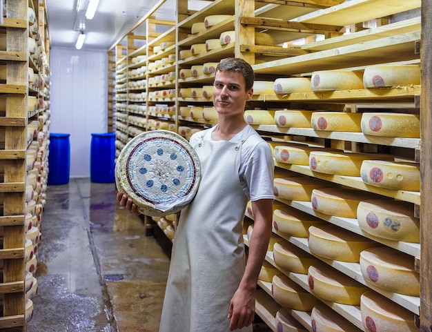 Evillers, Frankrijk - 31 augustus 2016: Werknemer houdt een wiel van Gruyere de Comte-kaas in rijpingskelder bij Franche Comte-creamery in Frankrijk