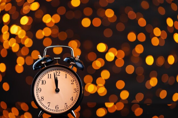 Ew year eve concept with alarm clock against blurred garland background