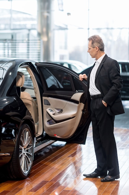 Examining car at dealership. Full length of confident mature man in formalwear opening the car door at the dealership