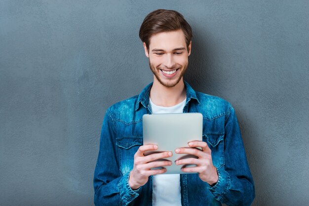 Examining his new gadget. Happy young man holding digital tablet and smiling