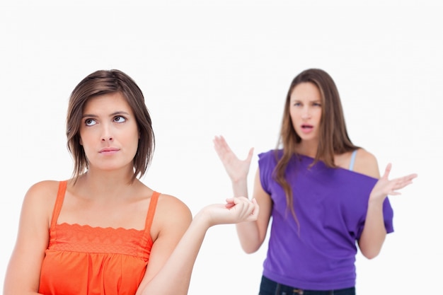 Exasperated teenager standing upright while her friend is roaring at her