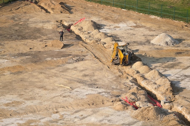 Excavator at the construction site dig trenches for cables and\
wires, while the work foreman stay ne