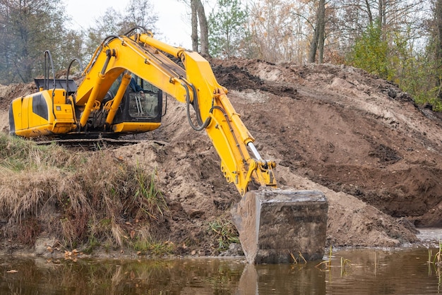 Excavator digging artificial water basin Long arm of an excavator spreading banks of a pond making it bigger