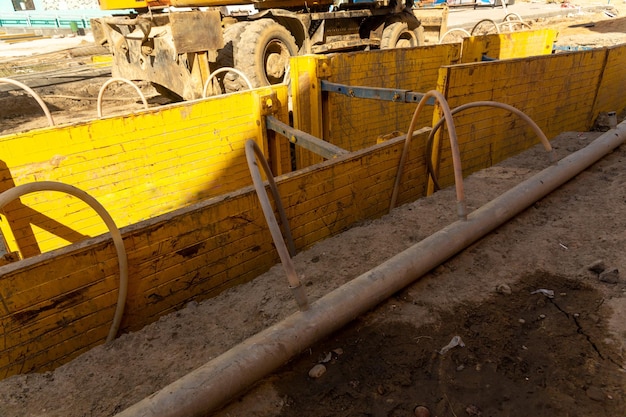 Excavator filling deep excavation supported by trench box with pipe bedding pea gravel during installation of drainage pipe