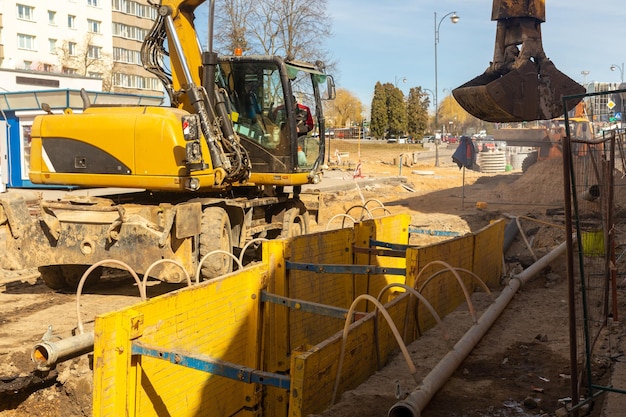 Excavator filling deep excavation supported by trench box with pipe bedding pea gravel during installation of drainage pipe