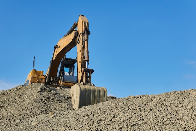 Excavator is standing on a pile of rubble against the background of the sky