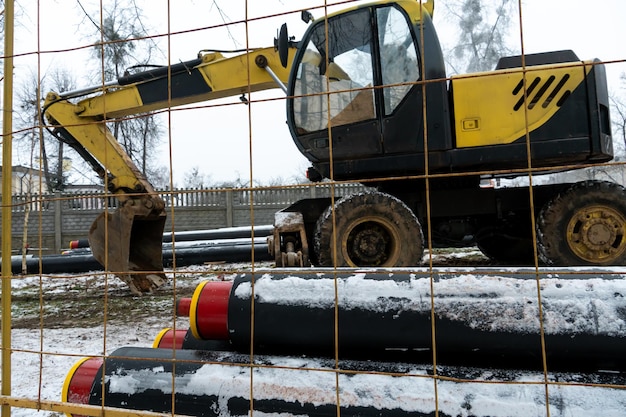 The excavator is working on the construction site to replace the pipeline in winter Digging holes for laying new pipes for central heating in a residential area