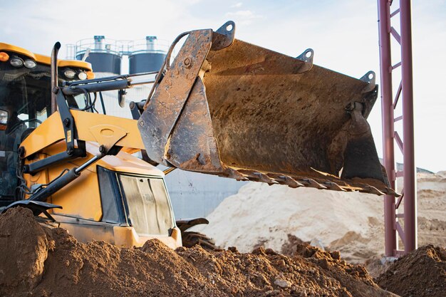 Экскаватор-погрузчик работает с ковшом для перевозки песка на строительной площадке. Профессиональная строительная техника для земляных работ.