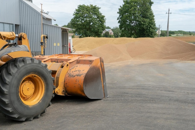 The excavator loads grain with a large bucket for processing and drying in the agro manufacturing plant of agricultural products Iron barrels with grain and grain silos of the Elevator Silver silos