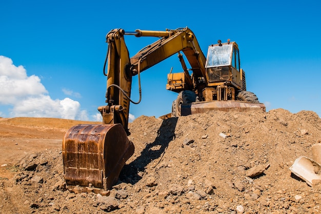 Excavator with bucket standing on soil hill and blue sky background