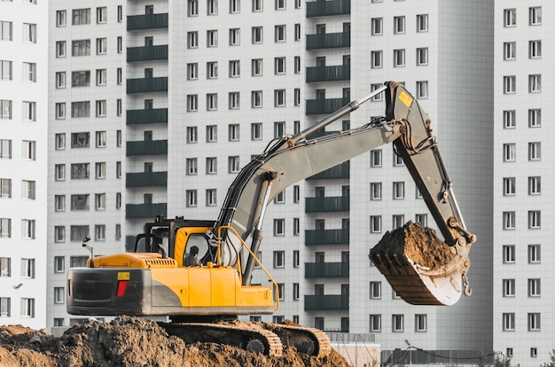 Excavator work on the ground on background of multi storey houses.