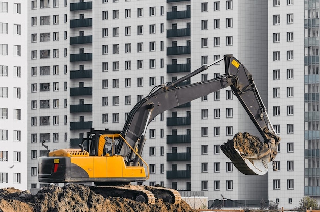 Excavator work on the ground on background of multi storey houses.