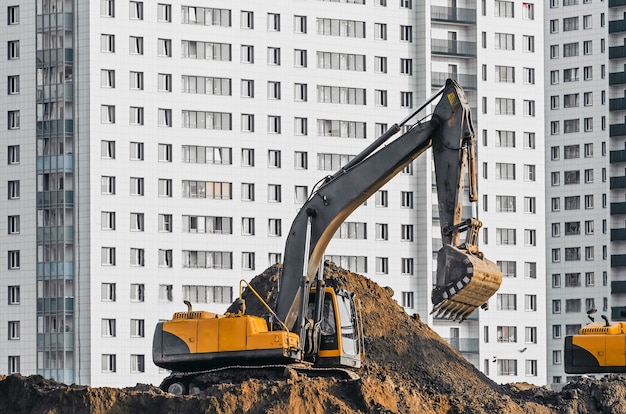 Excavator work on the ground on background of multi storey houses.