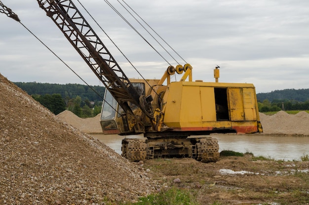 Excavator working in the river gravel quarry against the\
background of the forest extraction of natural resources