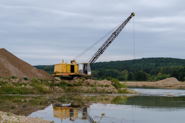 Excavator working in the river gravel quarry against the background of the forest Extraction of natural resources