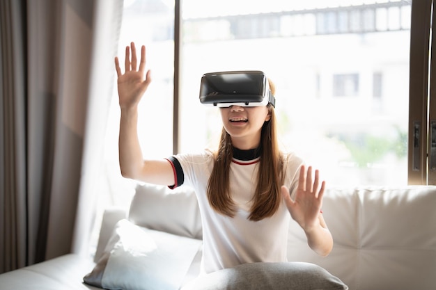 집에서 VR 안경과 컨트롤러로 온라인 게임을 하는 아시아 여성을 흥분시킨다