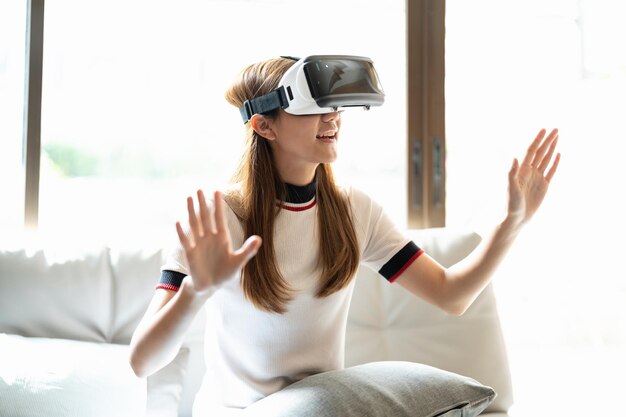 집에서 VR 안경과 컨트롤러로 온라인 게임을 하는 아시아 여성을 흥분시킨다