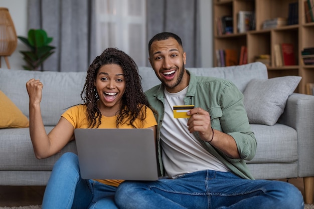 Excited african american couple with laptop and credit card celebrating success emotionally reacting