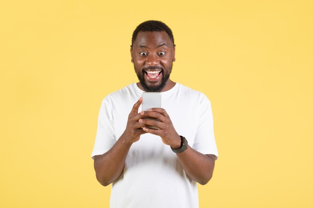 Excited African American Man Using Smartphone Playing Game Yellow Background