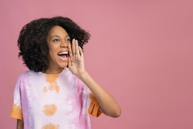 Excited African American woman holding hand near face screaming isolated on pink background