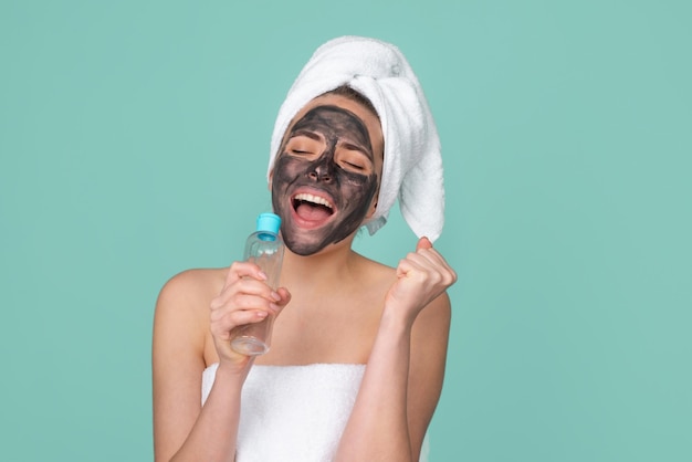 Excited amazed beautiful woman with cosmetic mud facial procedure, spa health concept. Skin care beauty treatment. Towel on head. Medical mineral mud.