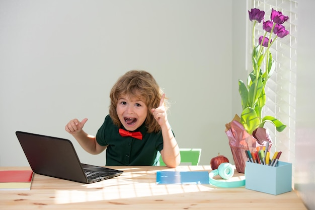 Excited amazed school boy doing homework little boy learns with laptop in study room