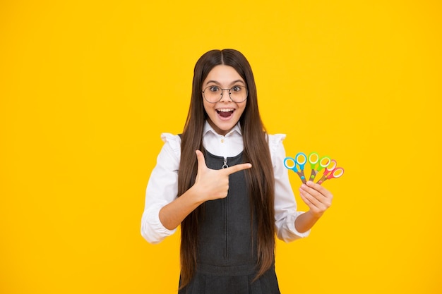 Excited amazed teenage girl with scissors isolated on yellow background Child creativity arts and crafts