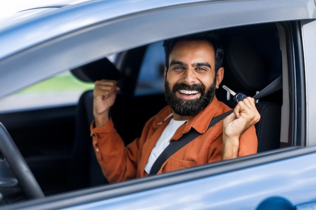 Excited arab driver man shaking clenched fists in car