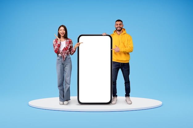 Excited arab man and asian woman standing by big phone