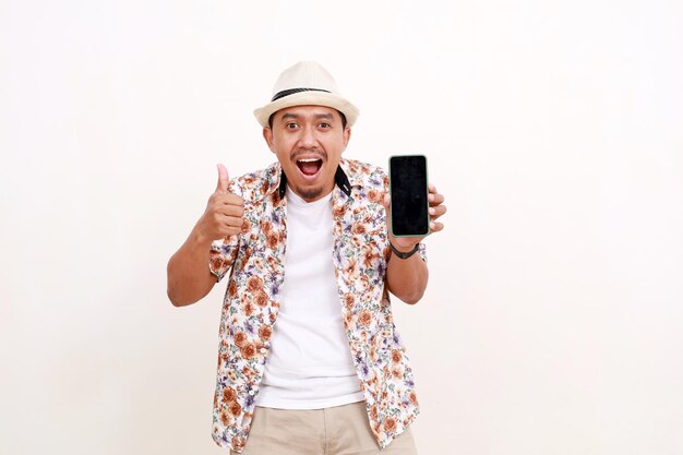 Excited asian adult man tourist making thumbs up while showing blank cell phone screen Concept of travel Isolated on white background