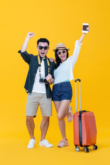 Excited Asian couple tourists with luggage raising hands up and yelling 