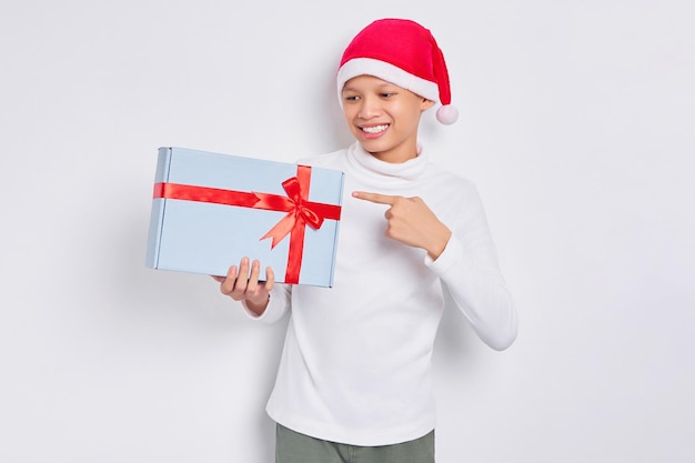 Eccitato uomo asiatico in cappello di natale che punta il dito su questo pacchetto di raccomandazione confezione regalo isolato su sfondo bianco concetto di pubblicità di natale