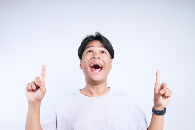 Excited Asian man looking and pointing up with both hands to empty space for ads or text