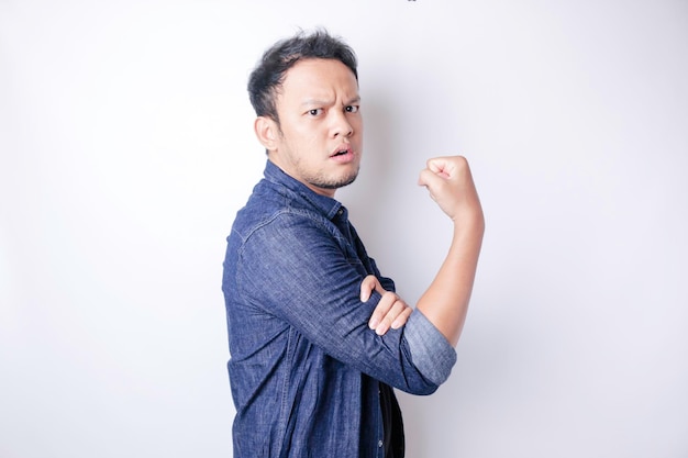 Excited Asian man wearing a navy blue shirt showing strong gesture by lifting his arms and muscles smiling proudly