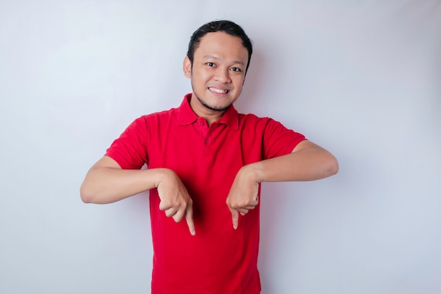 Excited Asian man wearing red tshirt pointing at the copy space below him isolated by white background