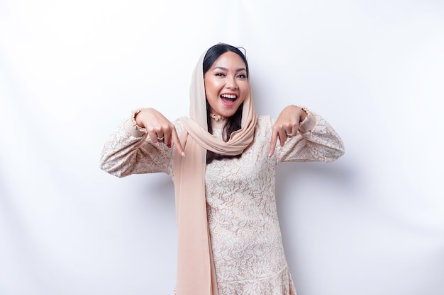 흰색 배경에 의해 고립된 그녀 아래 복사 공간을 가리키는 흥분한 아시아 무슬림 여성 히잡