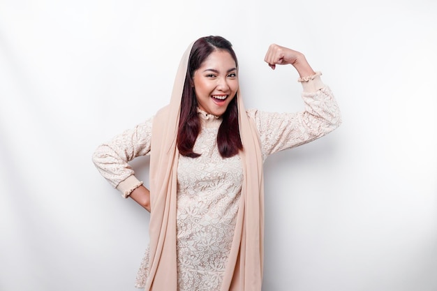 Excited Asian Muslim woman wearing a headscarf showing strong gesture by lifting her arms and muscles smiling proudly