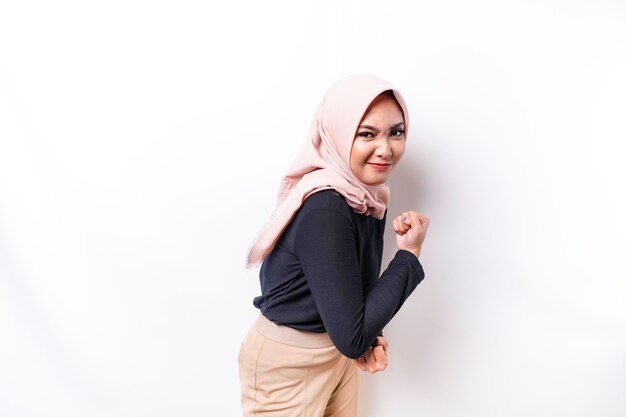 Excited Asian Muslim woman wearing a hijab showing strong gesture by lifting her arms and muscles smiling proudly